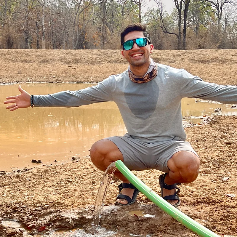 Suyash Keshari crouching by a newly filled waterhole, arms outstretched
